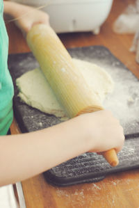 Midsection of woman pressing dough with rolling pin