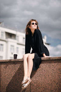 Beautiful young woman sitting on roof against sky