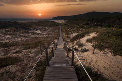 Footpath leading towards landscape against sky during sunset