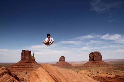 Man with cross-legged levitating over rock formation at monument valley against sky