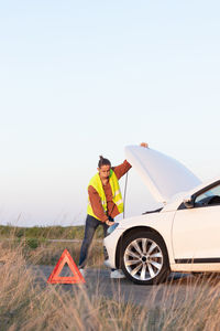 Side view of man standing by car against clear sky