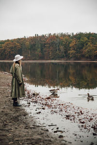 Side view of woman wearing hat standing by lake against sky