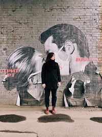 Full length of woman standing against graffiti wall