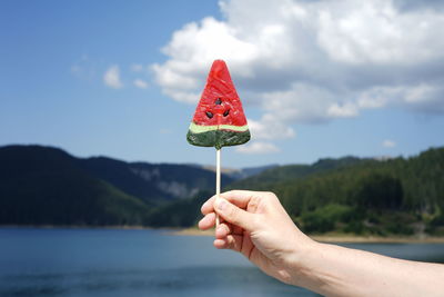 Close-up of hand holding lollipop against mountain
