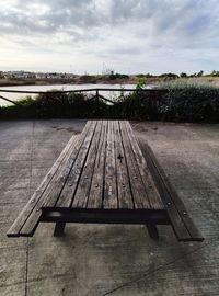 Empty bench on footpath by lake against sky