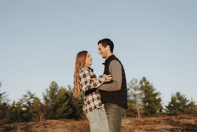 Young couple standing by tree against sky