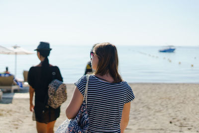 Rear view of women standing at beach against sky