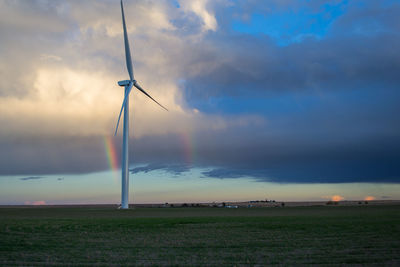 Wind turbines on field against cloudy sky