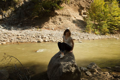 Young woman sitting on rock at riverbank
