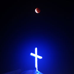 Low angle view of illuminated cross against blue sky