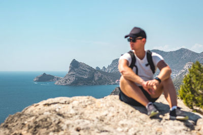 Man sitting on rock by sea against sky