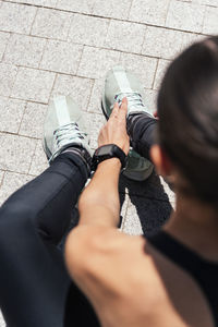 Confident slim female in activewear tying shoelaces on sneakers during training on sunny day in city