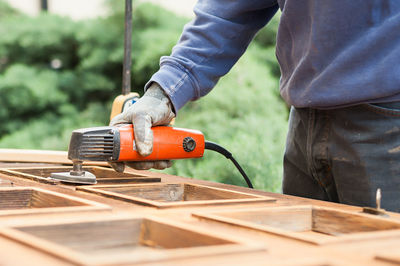 Close-up of man working with sander on wooden plank