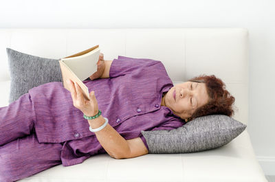 Woman reading book while lying on sofa at home