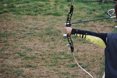 Midsection of person aiming with archery bow while standing on field