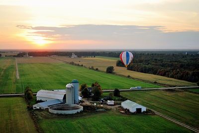 Hot air balloon flying over factory against sky during sunset