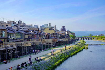 People on river by buildings in city against clear sky