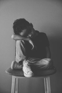 Full length of boy sitting on seat against wall