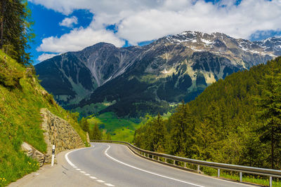 Road amidst trees and mountains against sky