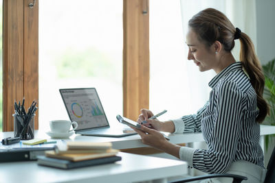 Side view of woman using laptop at office