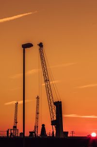 Low angle view of silhouette cranes against sky at sunset