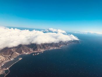 Aerial view of sea and mountains against blue sky