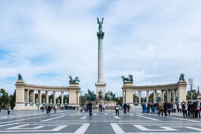 People at millennium monument against cloudy sky