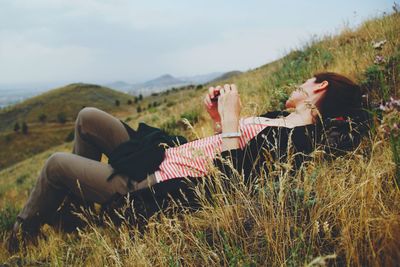 Young woman relaxing on grassy field against sky