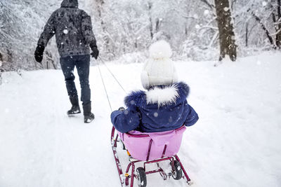 Dad takes his little daughter on a sledge uphill through the winter snow forest. active 