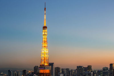 Illuminated tokyo tower amidst city against clear sky during sunset