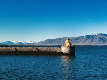 Scenic view of sea and mountains against clear blue sky