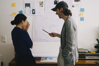 Happy multiracial architect colleagues discussing in front of blueprint on wall at home office