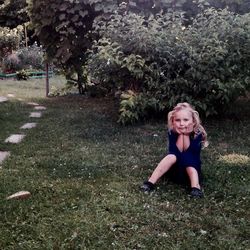 Portrait of cute girl sitting against plants on field at park