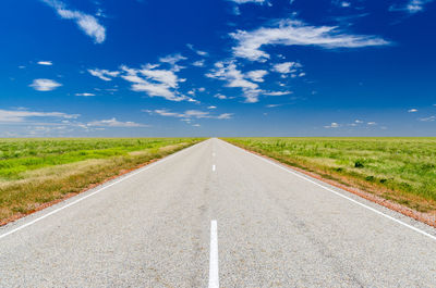 Road amidst green landscape against blue sky