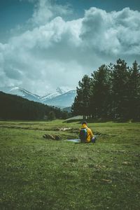 Rear view of man sitting on field against sky
