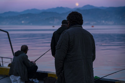 Rear view of man fishing at sea against sky