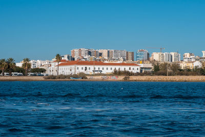 Buildings by sea against clear blue sky