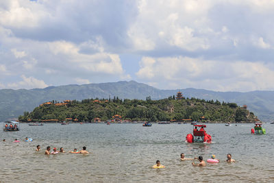 People enjoying in sea against cloudy sky