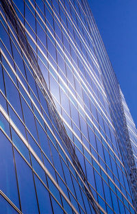 Low angle view of glass building against clear blue sky