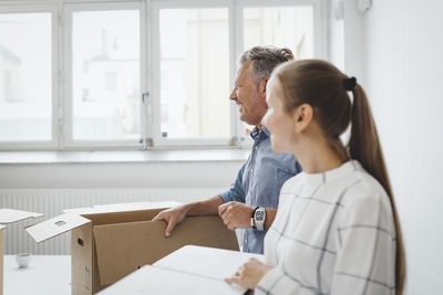Smiling mature businessman with cardboard box standing by female colleague in new office