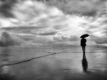 Silhouette boy standing on beach against sky