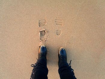 Low section of person standing with shoe prints at beach