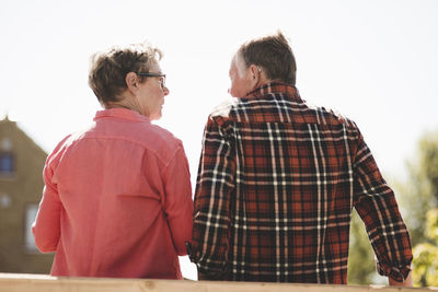 Rear view of senior couple looking at each other while standing against clear sky