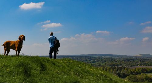 Man standing on field against sky with vizsla dog