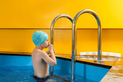Side view of boy sitting in swimming pool