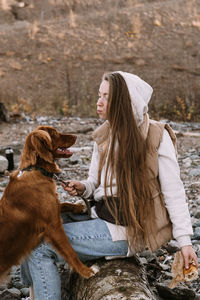 Young woman and dog retriever walks on river shore at autumn season