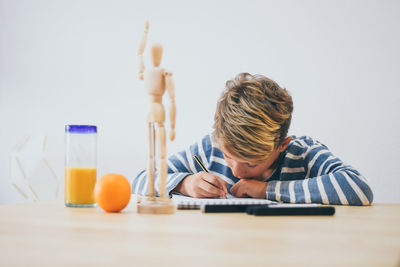 Boy drawing while sitting by table against wall