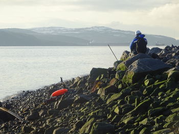 People on rock by sea against sky