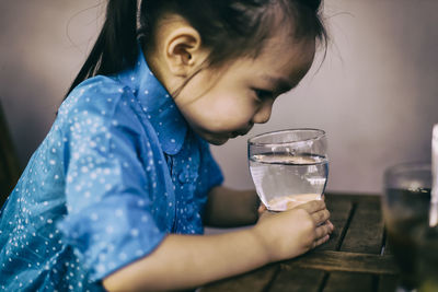 Close-up of girl drinking water in glass on table