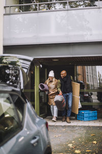 Mature couple with luggage walking towards car while leaving house